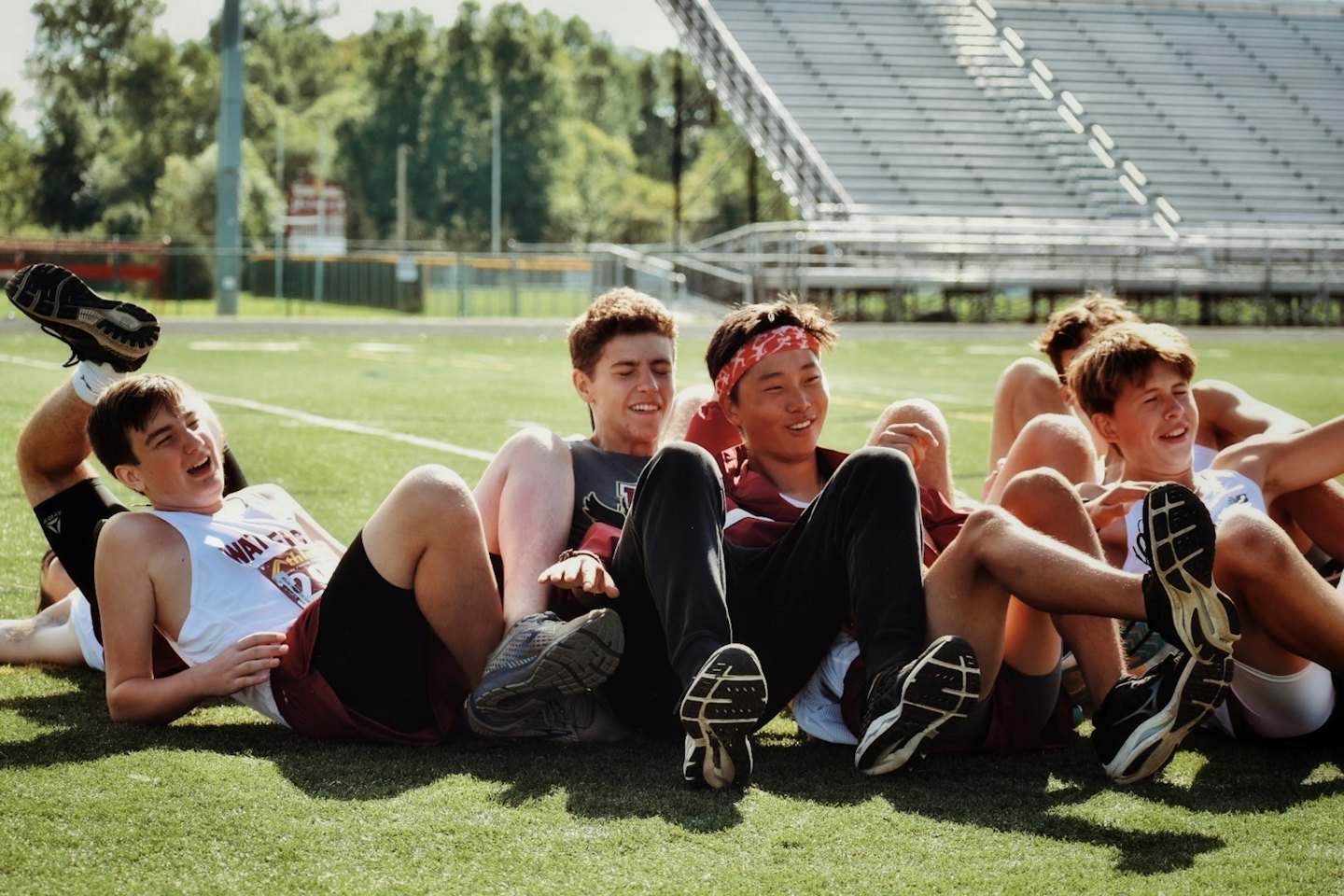 Five athletes resting on a green sports field after practice.