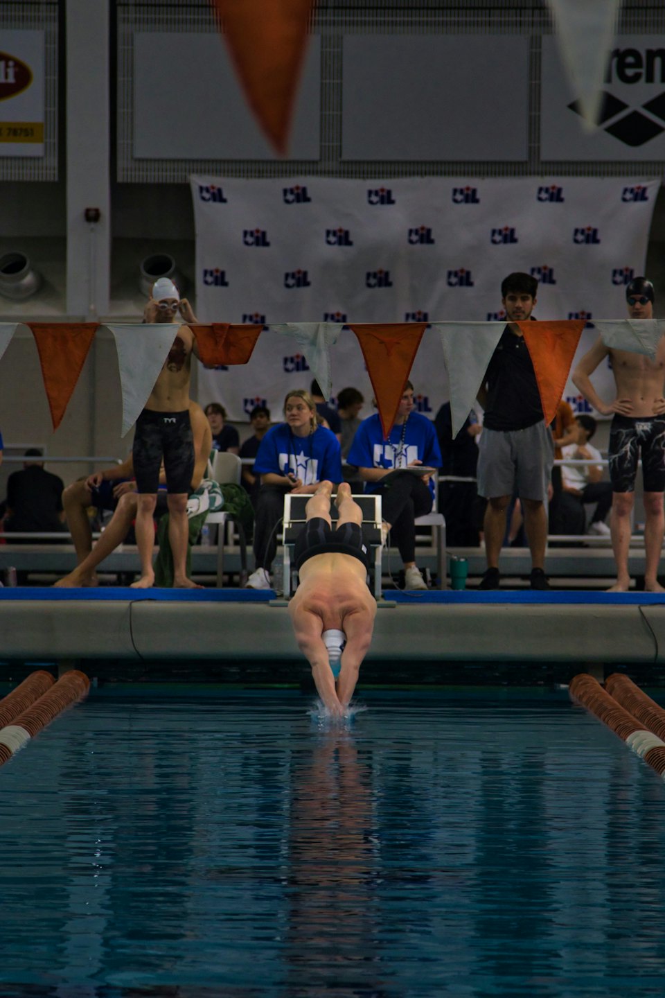 Male swimmer dives into indoor pool with a splash.