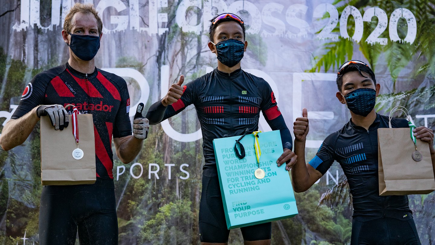 Athletes in masks and gear give thumbs-up with medals on a podium.
